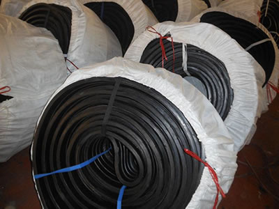 Many rolls of rubber waterstops wrapped with woven bags are on the ground.